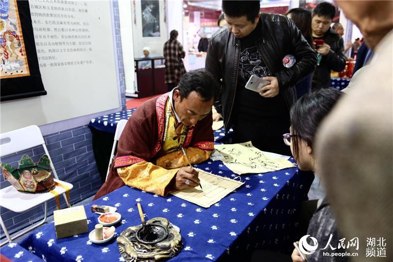 The 18th generation of successor of Yuannan Dongba culture writes pictograph for visitors. (Photo Source: people.cn)