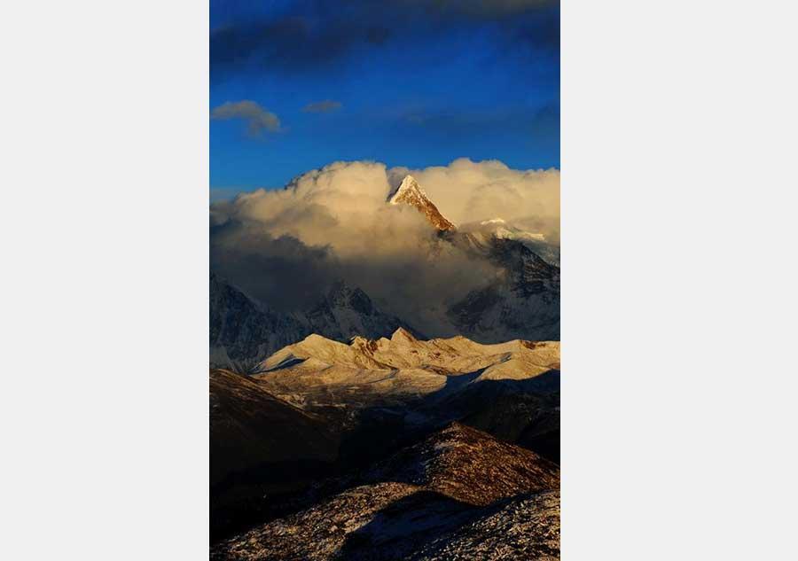 This photo taken on December 20, 2015 from the Sejila Mountain shows the winter scenery of the cloud-shrouded Namjagbarwa peak in Nyingchi, Tibet. The winter air in Nyingchi is fresh, with proper humidity, from the Sejila mountain pass which is at a latitude of 4728m, visitors can watch the stunning sunrise, as well as the mesmerizing view of the sea of clouds or forests. Although currently it is the slack season for tourism, there are still quite a number of visitors coming here to appreciate the unique scenery. Located at the Nyingchi prefecture in Tibet, Namjagbarwa, with an altitude of 7782m, is the fifteenth highest peak in the world. Since its giant triangular top is surrounded by mists and covered with snow all year long, the real appearance of the mountain is rarely seen, so it is nicknamed a "shy" mountain.[Photo/Xinhua]